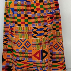 May include: A vibrant, patterned skirt and matching hat. The fabric features a patchwork design with orange, yellow, blue, green, and black geometric shapes. The skirt is long and flowing, and the hat is a round, brimmed style.