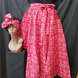 May include: A red skirt with a white geometric pattern. The skirt has a tie at the waist and is made of a lightweight fabric. The skirt is being modeled on a mannequin.