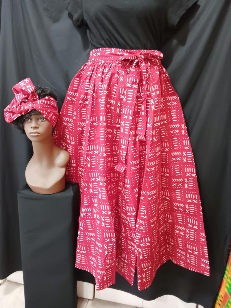 May include: A red skirt with a white geometric pattern. The skirt has a tie at the waist and is made of a lightweight fabric. The skirt is being modeled on a mannequin.