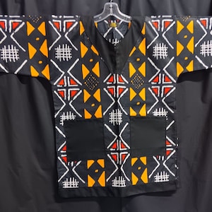 May include: A black short-sleeved shirt with a geometric pattern in white, yellow, and red. The shirt has two black pockets on the front.
