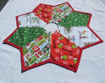 May include: A star-shaped Christmas tree skirt featuring a patchwork design of various Grinch-themed fabrics. The panels include red, green, and white patterns with illustrations of the Grinch, snowflakes, and text, all bordered by red fabric trim.