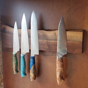 May include: A wooden magnetic knife holder with four knives. The knives have different colored handles, including green, blue, and brown. The holder is mounted on a wall.