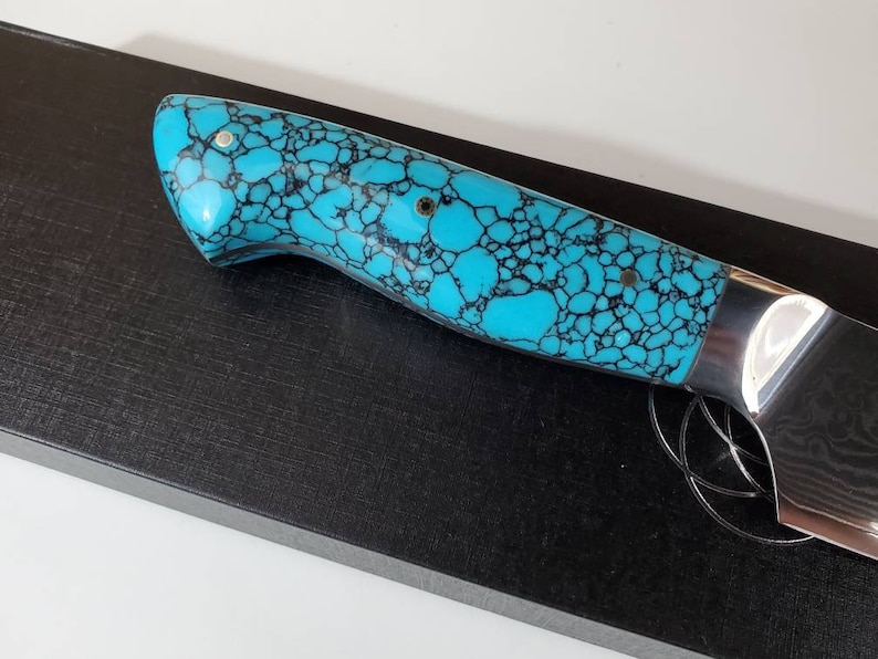 May include: A knife handle with a turquoise and black patterned design. The handle is made of a material that resembles turquoise.