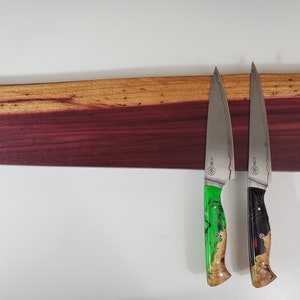 May include: A wooden knife holder with two chef's knives. The holder is a rectangular piece of wood, with a purple and brown color scheme. The knives have silver blades and green and black handles.