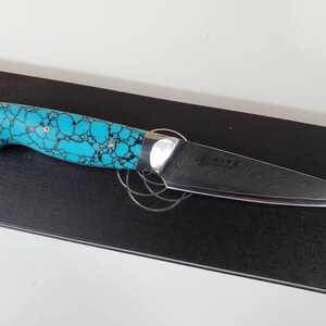 May include: A kitchen knife with a turquoise and black patterned handle and a Damascus steel blade.