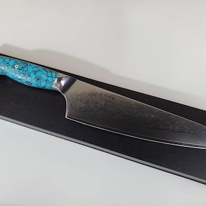 May include: A blue and silver chef's knife with a turquoise patterned handle. The knife is resting on a black surface.