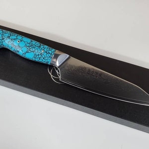 May include: A chef's knife with a turquoise and black patterned handle, a stainless steel blade and a Japanese inscription on the blade.