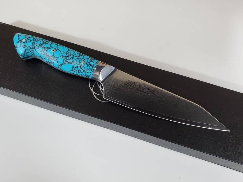 May include: A chef's knife with a turquoise and black patterned handle, a stainless steel blade and a Japanese inscription on the blade.