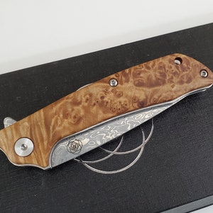 以下が含まれることがあります： 木製のハンドルとステンレススチール製のポケットナイフ。ダマスカスブレードが付いています。ハンドルは独特な模様で、シルバーの金属製のアクセントが付いています。