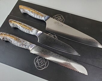 May include: Three kitchen knives with white and brown patterned handles. The top knife has a plain blade and the text "天寿作" on the blade. The middle knife has a wavy blade and the bottom knife has a serrated blade.