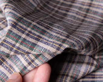 May include: Close-up of a beige, green, and blue plaid fabric with a hand holding the fabric.