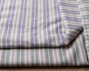 May include: Two pieces of striped fabric folded on top of each other. The top fabric is blue and white striped, and the bottom fabric is green and white striped.