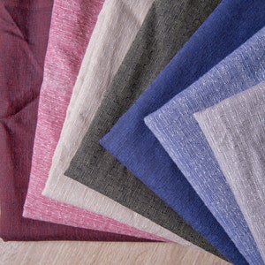 May include: A stack of fabric swatches in various colours, including burgundy, pink, beige, dark green, blue, and light grey. The fabric has a textured, woven appearance.