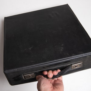 May include: A black leather carrying case with a silver handle. The case has a worn, vintage look.