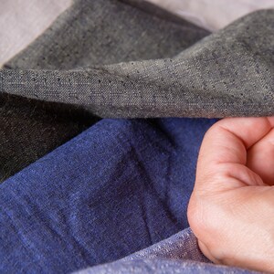 May include: Close-up of three different fabric swatches. The swatches are a dark grey, a light blue, and a light beige. The fabric is textured and has a woven appearance.