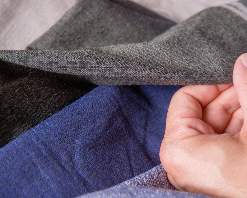 May include: Close-up of three different fabric swatches. The swatches are a dark grey, a light blue, and a light beige. The fabric is textured and has a woven appearance.