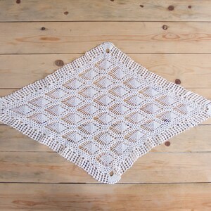 May include: White crocheted doily with a delicate pattern, laid flat on a wooden surface.
