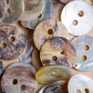 May include: A collection of various sized and patterned buttons made from mother of pearl and other natural materials. The buttons are in shades of brown, white, and cream.
