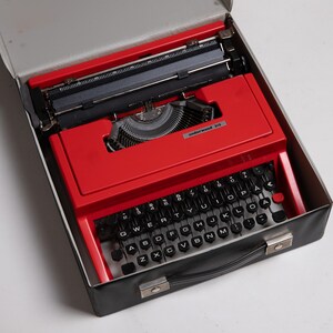 May include: A red vintage Underwood 318 portable typewriter in a black carrying case. The typewriter has a black keyboard with white lettering and a black carriage return lever.