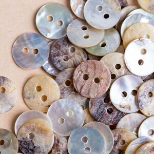 May include: A collection of various sized and patterned buttons made from mother of pearl and other natural materials. The buttons are in shades of white, brown, and beige.