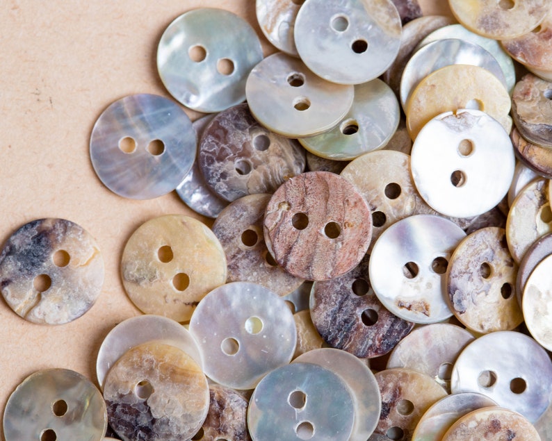 May include: A collection of various sized and patterned buttons made from mother of pearl and other natural materials. The buttons are in shades of white, brown, and beige.