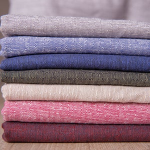 May include: A stack of seven fabric swatches in various colours and textures, including beige, blue, dark blue, green, light beige, pink, and burgundy.