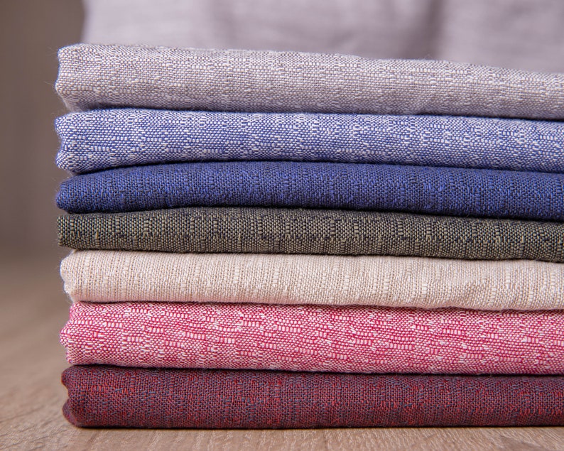 May include: A stack of seven fabric swatches in various colours and textures, including beige, blue, dark blue, green, light beige, pink, and burgundy.