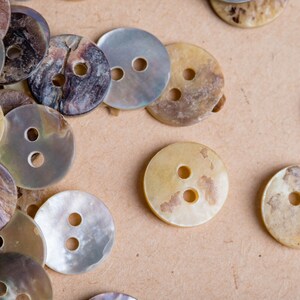 May include: A collection of various sized, two-hole, mother-of-pearl buttons in shades of brown, beige, and white. The buttons have a smooth, shiny finish.