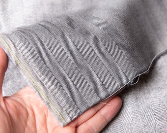 May include: Close-up of a gray herringbone fabric with a visible seam. The fabric is folded over and held in a hand.
