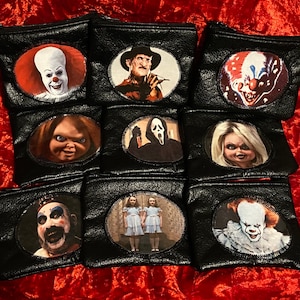 May include: Nine black zippered pouches with round, colorful patches featuring horror movie characters. The characters include Freddy Krueger, Pennywise, Chucky, Ghostface, and the twins from The Shining.