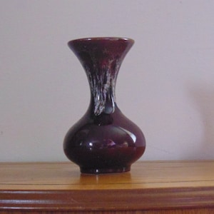 May include: A dark purple ceramic vase with white streaks of glaze. The vase has a narrow neck and a round body.