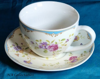 May include: A white teacup and saucer with a floral pattern in shades of pink, purple, and yellow. The cup and saucer have a blue and gold trim.