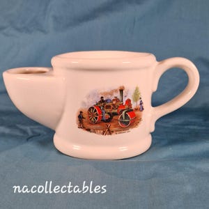 May include: A white ceramic shaving mug with a handle and a built-in soap dish. The mug features a colorful illustration of a steam roller with people and trees. The text "Steam Roller by Aveling 1891" is below the illustration.
