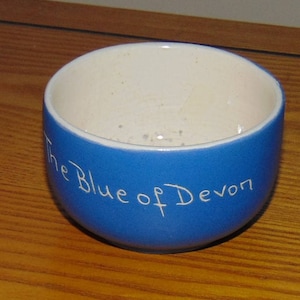 May include: A blue ceramic cup with white lettering that reads "The Blue of Devon".
