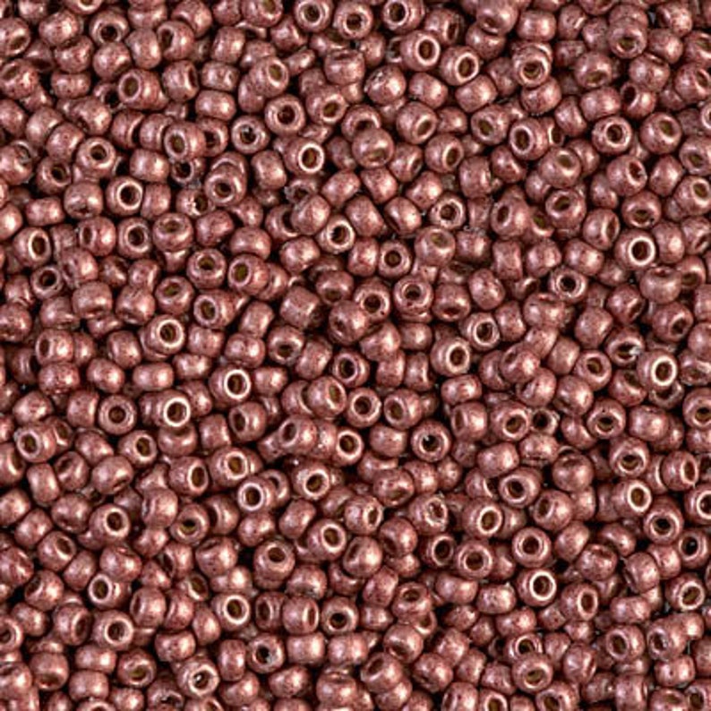 May include: A close-up view of a large quantity of small, round, metallic beads. The beads are a deep rose gold color with a slightly textured surface.