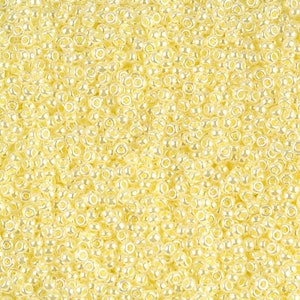 May include: A close-up image of a large quantity of small, round, cream-colored glass beads. The beads have a slight iridescent sheen.