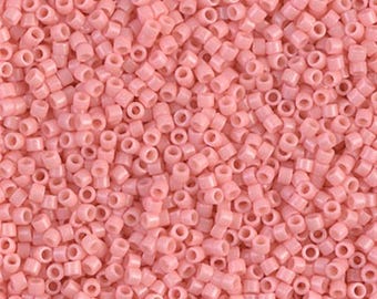 May include: A close-up image of a large quantity of small, pink seed beads. The beads are opaque and have a slightly glossy finish.