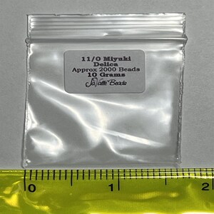 May include: A clear plastic bag containing 11/0 Miyuki Delica beads. The bag has a label that reads "11/0 Miyuki Delica Approx 2000 Beads 10 Grams JaVaTe Beads".