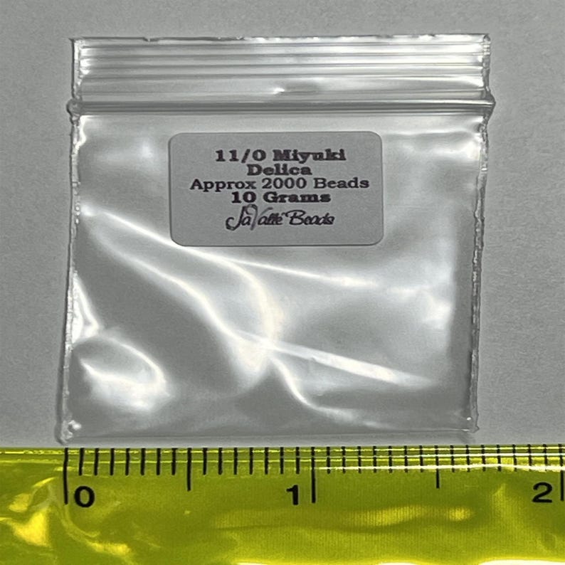 May include: A clear plastic bag containing 11/0 Miyuki Delica beads. The bag has a label that reads "11/0 Miyuki Delica Approx 2000 Beads 10 Grams JaVaTe Beads".