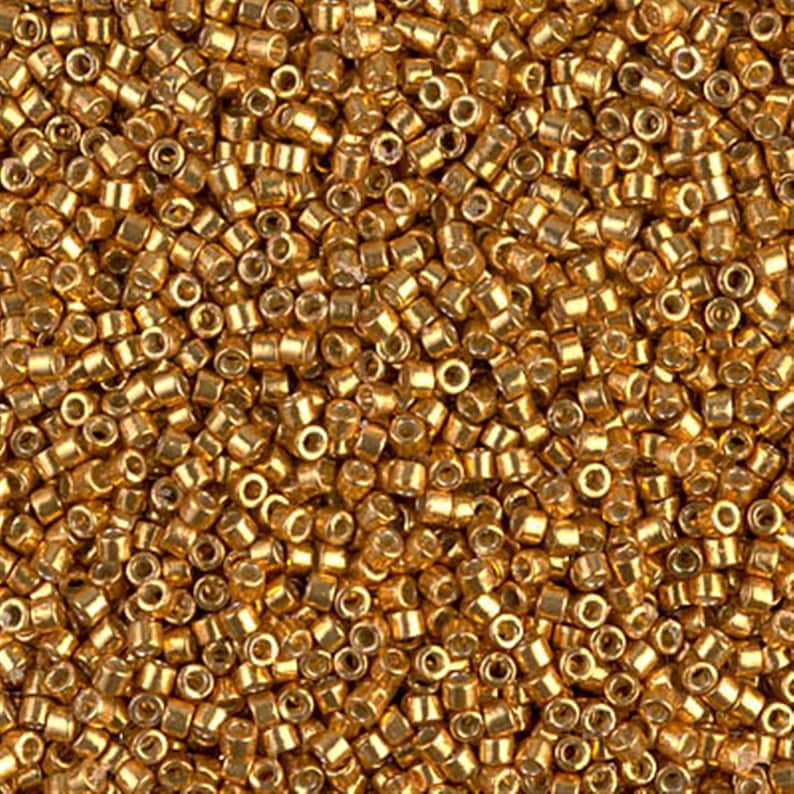 Puede incluir: Vista de cerca de una gran cantidad de peque&ntilde;as cuentas de semillas doradas. Las cuentas son redondas y tienen un acabado brillante y met&aacute;lico.