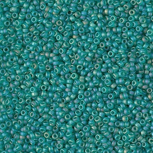 May include: A close-up view of a large quantity of teal-colored glass seed beads. The beads are small and round with a slight iridescent sheen.