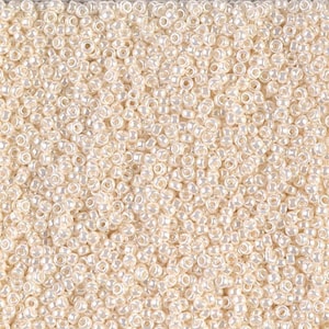 May include: A close-up image of a large quantity of small, white, round seed beads. The beads have a slight iridescent sheen.