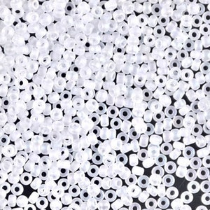 May include: A close-up view of a large quantity of small, white, opaque seed beads. The beads are round with a hole in the center.