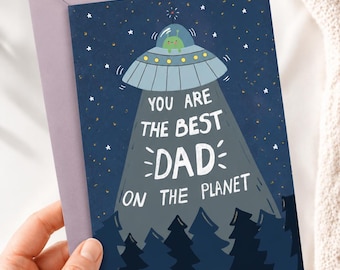 Könnte beinhalten: Eine Grußkarte mit einem lila Umschlag. Die Karte zeigt einen blauen Nachthimmel mit Sternen, ein UFO mit einem Alien und den Text "YOU ARE THE BEST DAD ON THE PLANET". Darunter sind dunkelblaue Bäume.