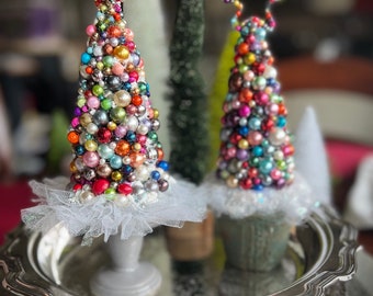 May include: Two miniature Christmas trees decorated with colorful beads and ornaments on a silver tray. The trees are topped with a star and a gold bead.