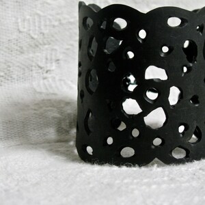 K&ouml;nnte beinhalten: Schwarzes Spitzen-Armband mit gewelltem Rand. Das Armband ist aus flexiblem Material gefertigt und hat ein zartes, filigranes Design.