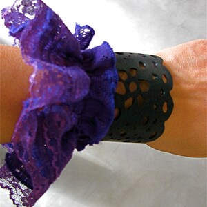 K&ouml;nnte beinhalten: Ein schwarzes Lederarmband mit einem spitzem Design, verziert mit einer violetten Spitzenr&uuml;sche.