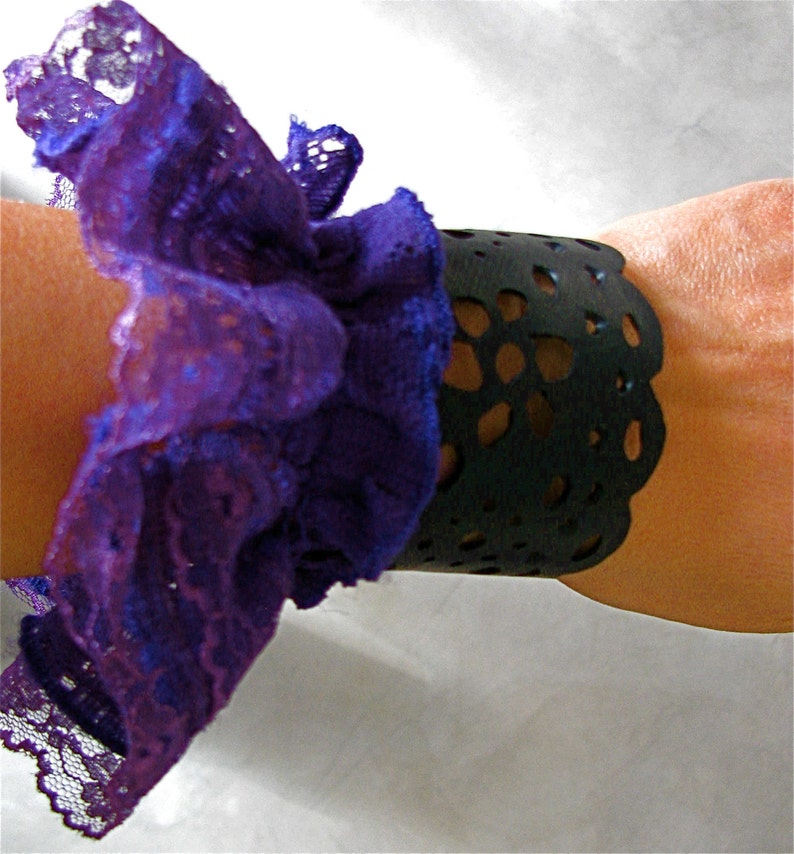 K&ouml;nnte beinhalten: Ein schwarzes Lederarmband mit einem spitzem Design, verziert mit einer violetten Spitzenr&uuml;sche.