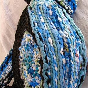 Pu&ograve; includere: Un tappeto all'uncinetto blu e bianco realizzato con sacchetti di plastica riciclati. Il tappeto ha una forma circolare e un bordo nero.