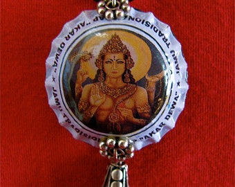 Può includere: Una collana con un ciondolo d'argento e un tappo di bottiglia bianco con un'immagine colorata di una divinità. Il tappo della bottiglia ha il testo "JAMU TRADISIONAL AKAR DEWA...", e il ciondolo ha la forma di una lacrima d'argento.